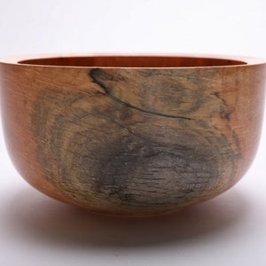 May include: A large, wooden bowl with a natural, brown and gray wood grain pattern. The bowl is round and has a smooth, polished finish.