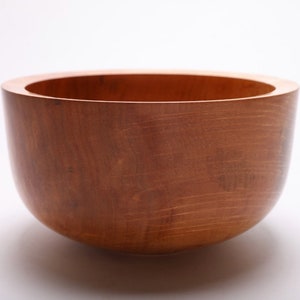 May include: A large, wooden bowl with a natural, reddish-brown finish. The bowl is round and has a smooth, slightly curved surface.