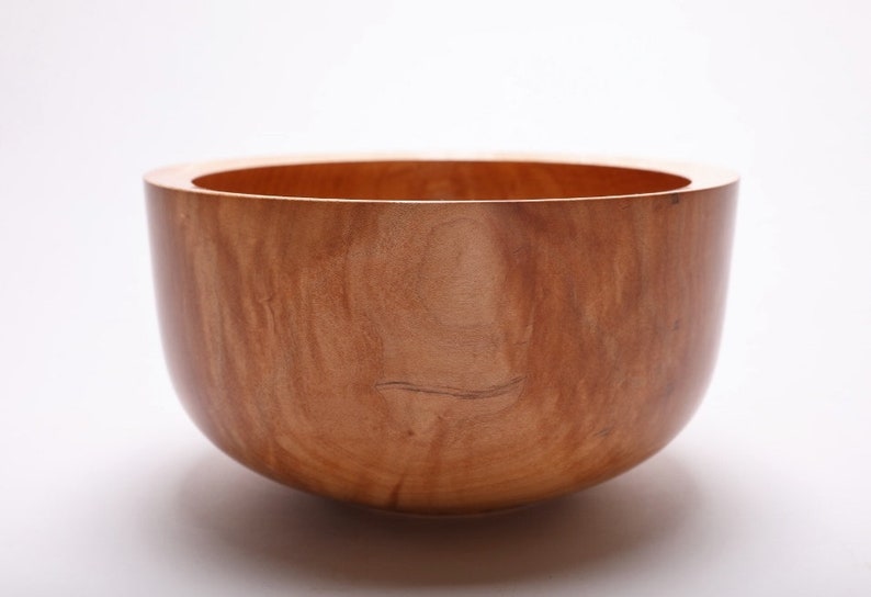 May include: A large, wooden bowl with a natural, reddish-brown finish. The bowl is made from a single piece of wood and has a smooth, rounded shape.