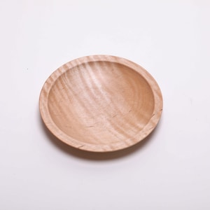 May include: A small, round wooden bowl with a natural wood finish. The bowl has a slightly raised rim and a smooth, polished surface.