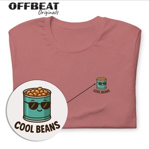 May include: Dusty rose t-shirt with a small cartoon graphic of a can of beans wearing sunglasses and the text "COOL BEANS". The shirt also has a larger graphic of the same design. The brand name "OFFBEAT Originals" is at the top.