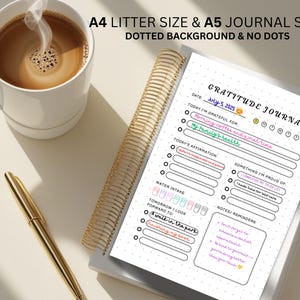 May include: A gratitude journal with a gold spiral binding, a cup of coffee, and a gold pen. The journal is open to a page with the title "Gratitude Journal" and prompts for daily reflections. The text "A4 Litter Size & A5 Journal Size" is at the top.