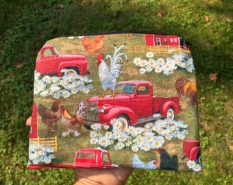 May include: A rectangular zippered pouch with a farm scene print. The design features red pickup trucks, white daisies, chickens, and a rooster. The background is a mix of green and brown.