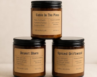 May include: Three amber glass jars with black lids, each containing an 8 oz soy wax candle. The labels are tan paper with black text reading Cabin In The Pines, Desert Shore, and Spiced Driftwood, listing scent notes and production details.
