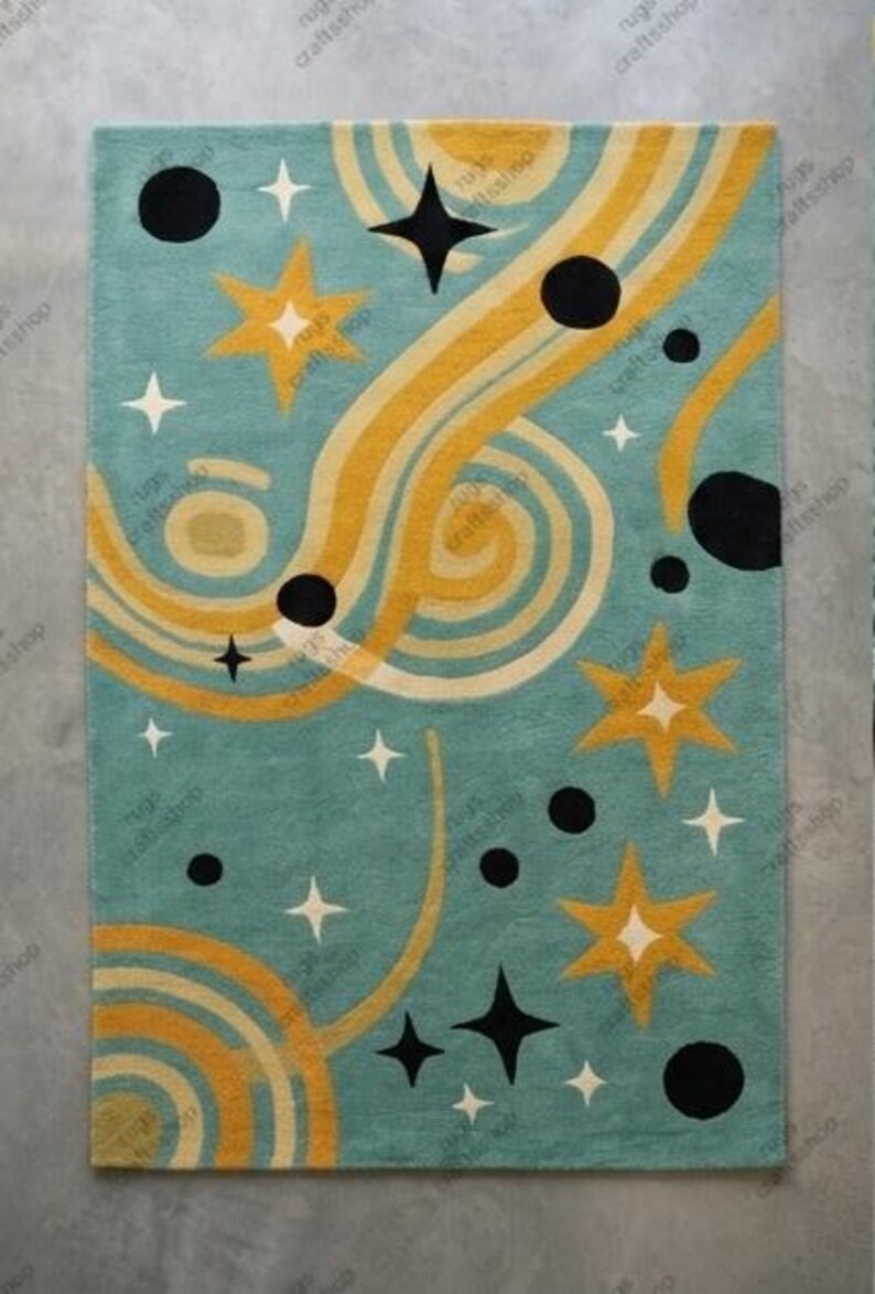 May include: A rectangular rug with a teal background featuring a retro design. The rug has yellow and cream-colored wavy lines, black circles, and star shapes in white, yellow, and black. The rug is a decorative home accent.
