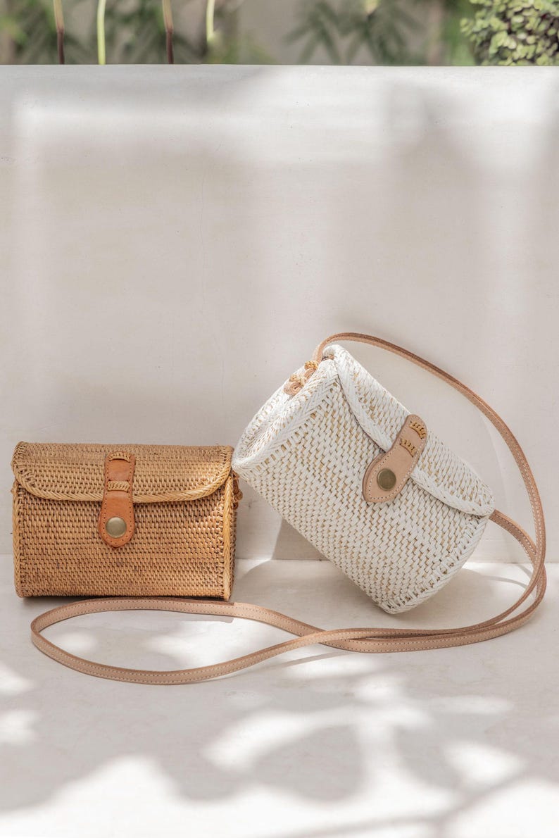 Two handbags, one brown and one white, are placed on a white surface against a white wall.