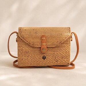 A woven purse with a leather strap, sitting on a white surface against a plain background.