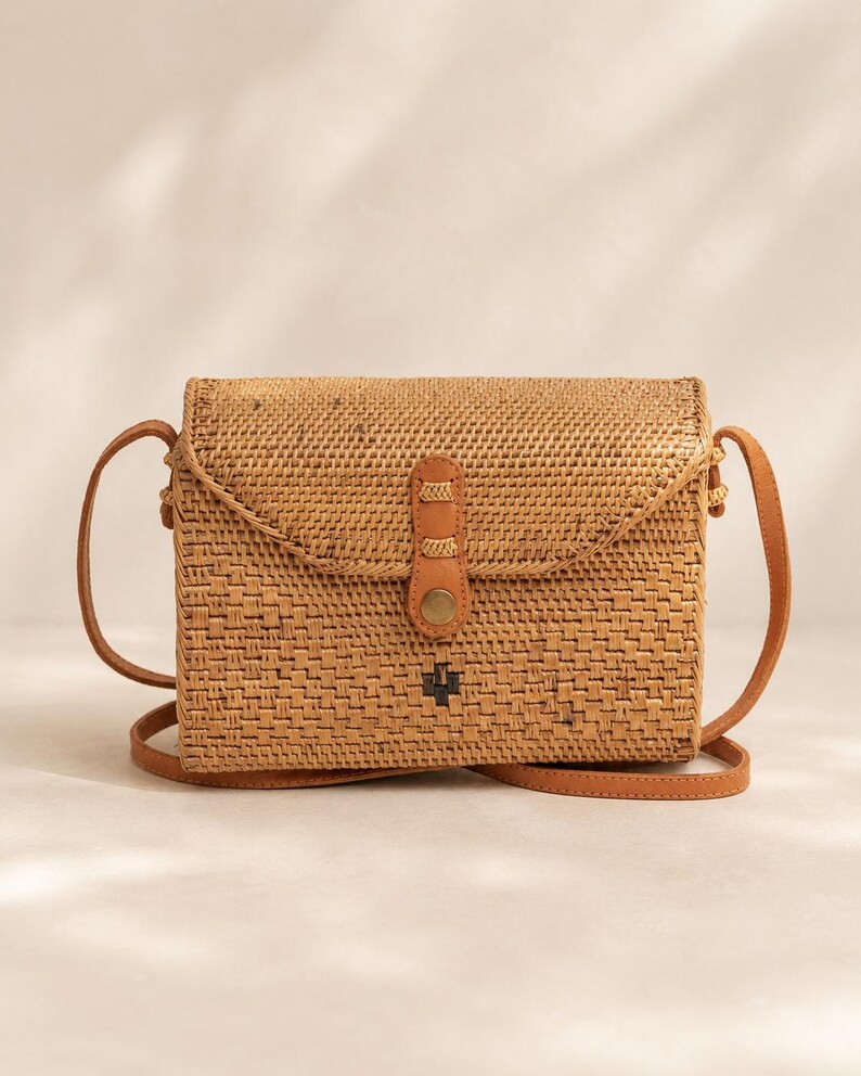 A woven purse with a leather strap, sitting on a white surface against a plain background.