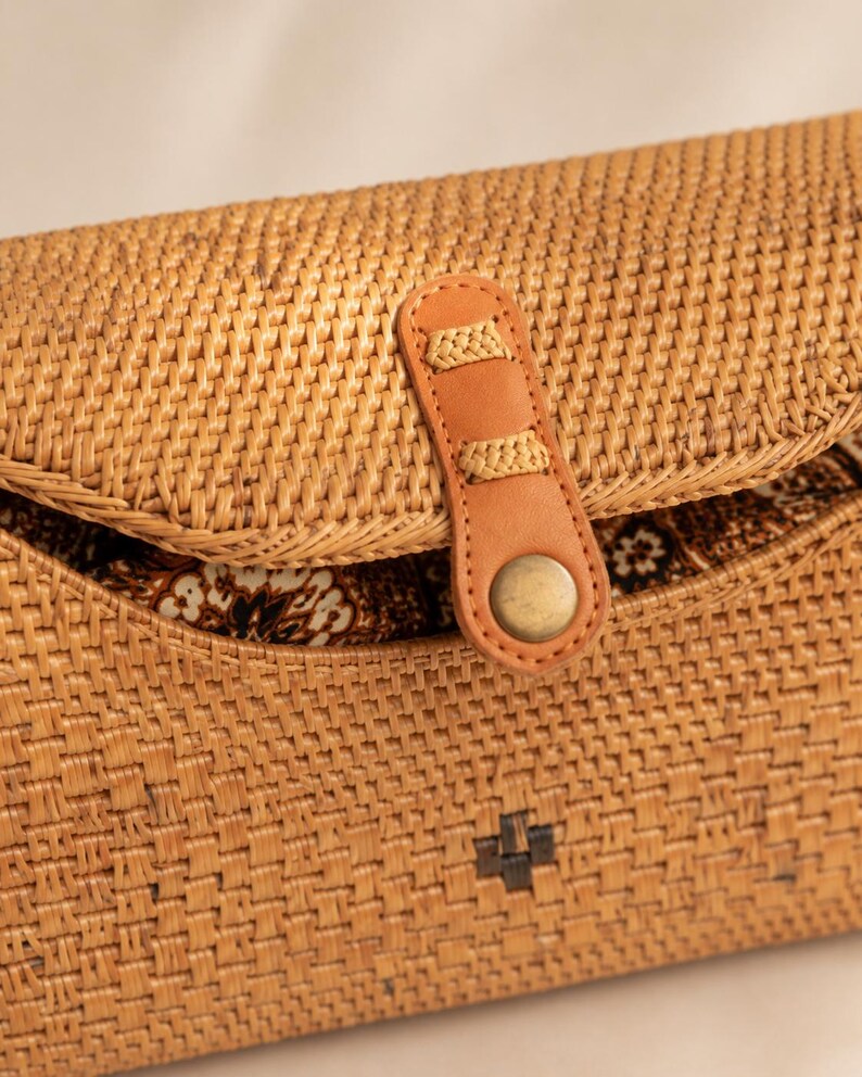 A close-up image of a woven straw bag with a leather strap and a metal button.