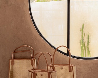May include: Three structured tote bags crafted from light beige woven cane webbing with tan leather trim and matching top handles. The bags feature a square base and open top design, showcasing a consistent grid pattern throughout the material.