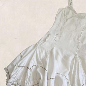 K&ouml;nnte beinhalten: Ein wei&szlig;es &auml;rmelloses Kleid mit einem figurbetonten Oberteil mit sichtbaren N&auml;hten und einem ausgestellten Rock. Der Rock besteht aus mehreren Bahnen und horizontalen Steppn&auml;hten und endet in einem R&uuml;schensaum mit d&uuml;nnen braunen Akzenten.