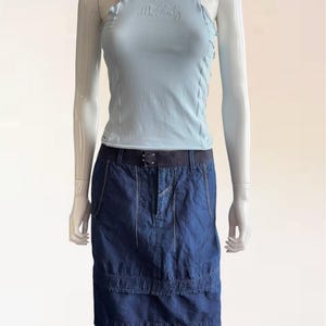 Puede incluir: Una camiseta sin mangas azul claro con el texto bordado "Mr. Judy" combinada con una falda vaquera azul oscuro. La falda tiene un cinturón oscuro y detalles de costura blancos. El conjunto se muestra en un maniquí.