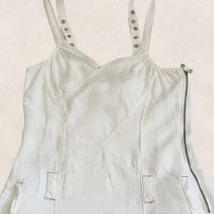 K&ouml;nnte beinhalten: Ein wei&szlig;es &auml;rmelloses Kleid mit V-Ausschnitt, breiten Schultertr&auml;gern mit silberfarbenen Metalldruckkn&ouml;pfen und einem auff&auml;lligen seitlichen Rei&szlig;verschluss. Das Kleidungsst&uuml;ck verf&uuml;gt &uuml;ber vertikale Nahtdetails und zwei kleine rechteckige Taschen.