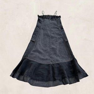 Könnte beinhalten: Ein dunkelblaues Jeans-Maxikleid mit Spaghettiträgern und einem gerüschten Ausschnitt. Das Kleid hat ein figurbetontes Oberteil, einen ausgestellten Rock und einen kontrastierenden dunklen Stoffeinsatz am Saum. Das Kleid hat zwei kleine Taschen.