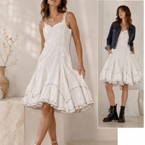 K&ouml;nnte beinhalten: Ein wei&szlig;es &auml;rmelloses knielanges Kleid mit eckigem Ausschnitt, breiten Tr&auml;gern und einem ausgestellten Rock mit ger&uuml;schtem Saum und dunklen Kontrastn&auml;hten. Das Kleid hat ein figurbetontes Oberteil und einen seitlichen Rei&szlig;verschluss.