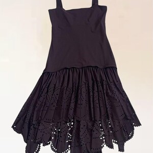 Könnte beinhalten: Schwarzes Kleid mit quadratischem Ausschnitt und Spaghettiträgern. Das Kleid hat einen gestuften Rock mit gewelltem Saum und aufwendigen Cut-Out-Details. Hergestellt aus leichtem Stoff, perfekt für warme Tage.
