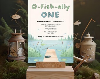 Peut inclure: Une invitation d'anniversaire avec le texte "O-fish-ally ONE" et une illustration sur le thème de la pêche. L'invitation comprend les détails d'une fête de premier anniversaire, avec une scène de lac et un ponton en bois. L'invitation est affichée sur un support en bois.
