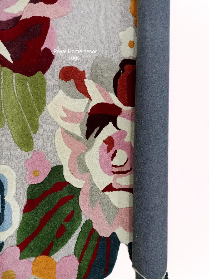 May include: A rolled-up floral rug with a gray backing. The rug features large, colorful flowers in shades of pink, red, green, and white. The text "Royal Home decor rugs" is visible on the rug.