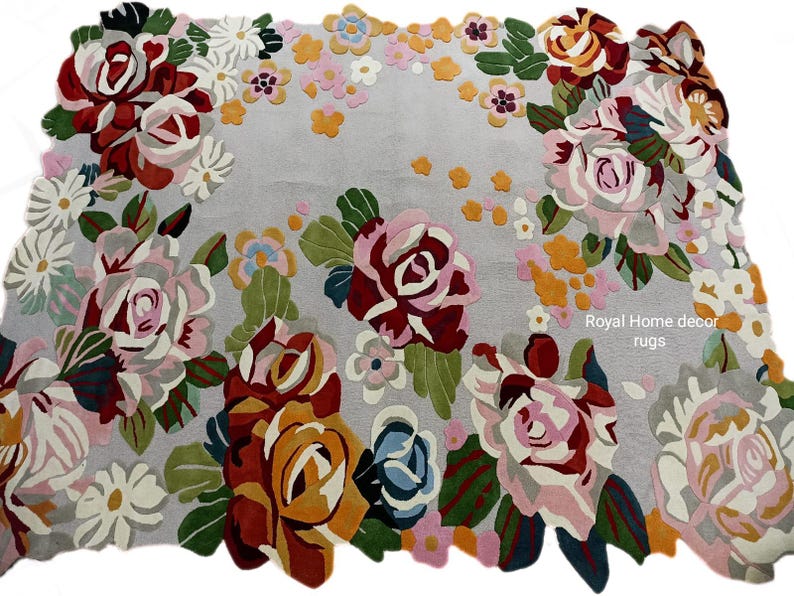 May include: A rectangular rug with a light gray background and a floral design. The rug features large roses in shades of red, pink, and yellow, with green leaves. Smaller flowers in pink, white, and orange are scattered throughout the design. The text "Royal Home decor rugs" is visible.