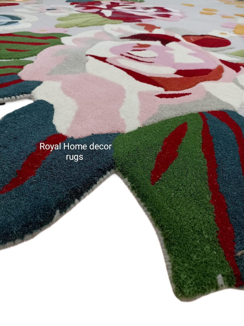 May include: A close-up of a floral rug with a light gray background. The rug features large, stylized flowers in shades of pink, red, white, and green. The text "Royal Home decor rugs" is visible on the rug.