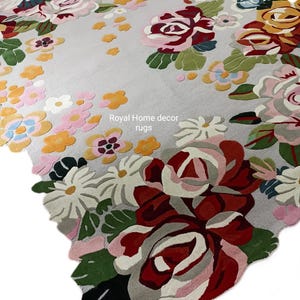 May include: A floral area rug with a light gray background and a colorful pattern of roses and other flowers. The rug features shades of red, pink, yellow, and green. The text "Royal Home decor rugs" is visible.