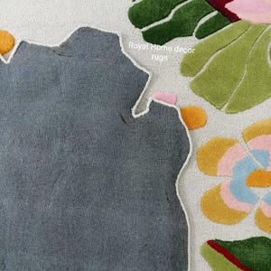 May include: A close-up of a floral rug with a gray, irregular shape. The rug features colorful floral designs in pink, yellow, blue, and green against a white background. The text "Royal Home decor rugs" is visible.