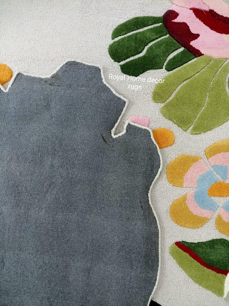 May include: A close-up of a floral rug with a gray, irregular shape. The rug features colorful floral designs in pink, yellow, blue, and green against a white background. The text "Royal Home decor rugs" is visible.
