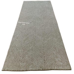 May include: A rectangular, neutral-toned rug with a herringbone pattern. The rug features a repeating V-shaped design in shades of beige and off-white. The text "Royal Home decor rugs" is visible on the rug.