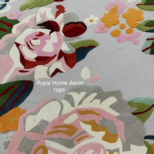 May include: A floral rug featuring large, detailed rose designs in shades of pink, red, white, and gray, with green leaves and yellow accents. The rug has a light gray background and the text "Royal Home decor rugs".