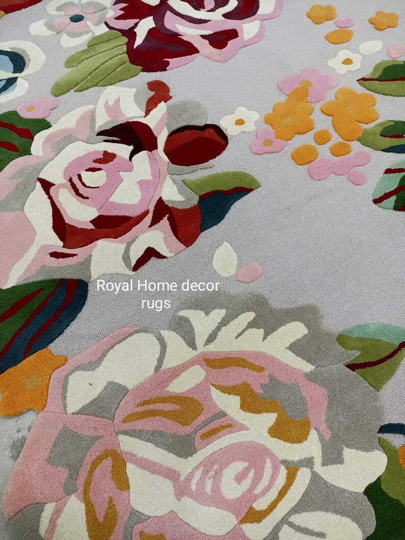 May include: A floral rug featuring large, detailed rose designs in shades of pink, red, white, and gray, with green leaves and yellow accents. The rug has a light gray background and the text "Royal Home decor rugs".