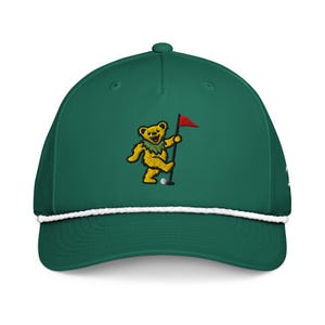 May include: A green baseball cap with a white rope detail and a yellow bear embroidered on the front. The bear is holding a golf flag and a golf ball. The cap has a curved brim.