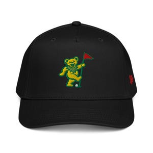May include: Black baseball cap featuring an embroidered yellow bear playing golf. The bear has a green collar and is holding a red flag. The cap has a curved brim and a small red logo on the side.
