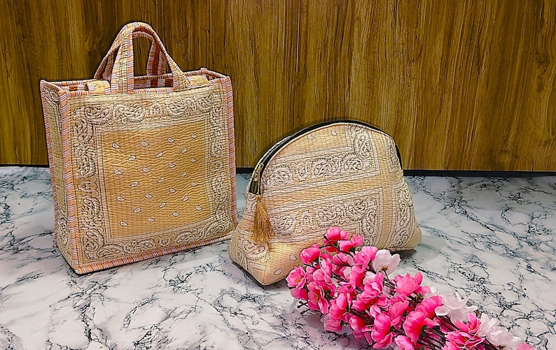May include: A tote bag and a cosmetic bag with a matching paisley pattern in beige and pink. The tote bag has two handles and the cosmetic bag has a zipper closure. A bouquet of pink flowers is in the foreground.
