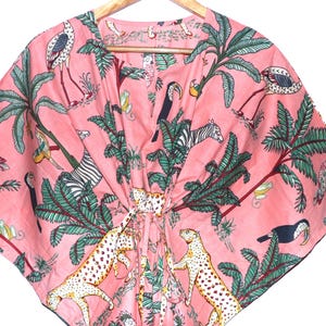 Op de afbeelding: Roze kaftan met een tropische print met palmbomen, zebra's, luipaarden, toekans en andere vogels. De kaftan heeft een V-hals en een trekkoordsluiting. De stof is lichtgewicht en lijkt van katoen te zijn.