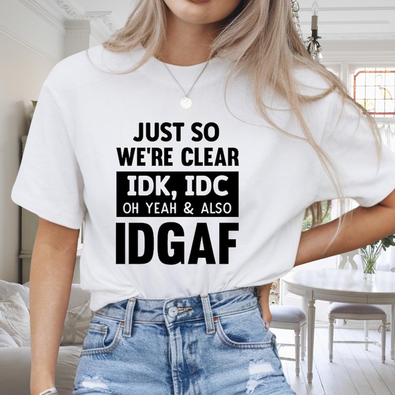May include: White t-shirt with black text that reads "JUST SO WE'RE CLEAR IDK, IDC OH YEAH & ALSO IDGAF". The shirt is paired with blue denim jeans. The top is a casual, everyday wear item.