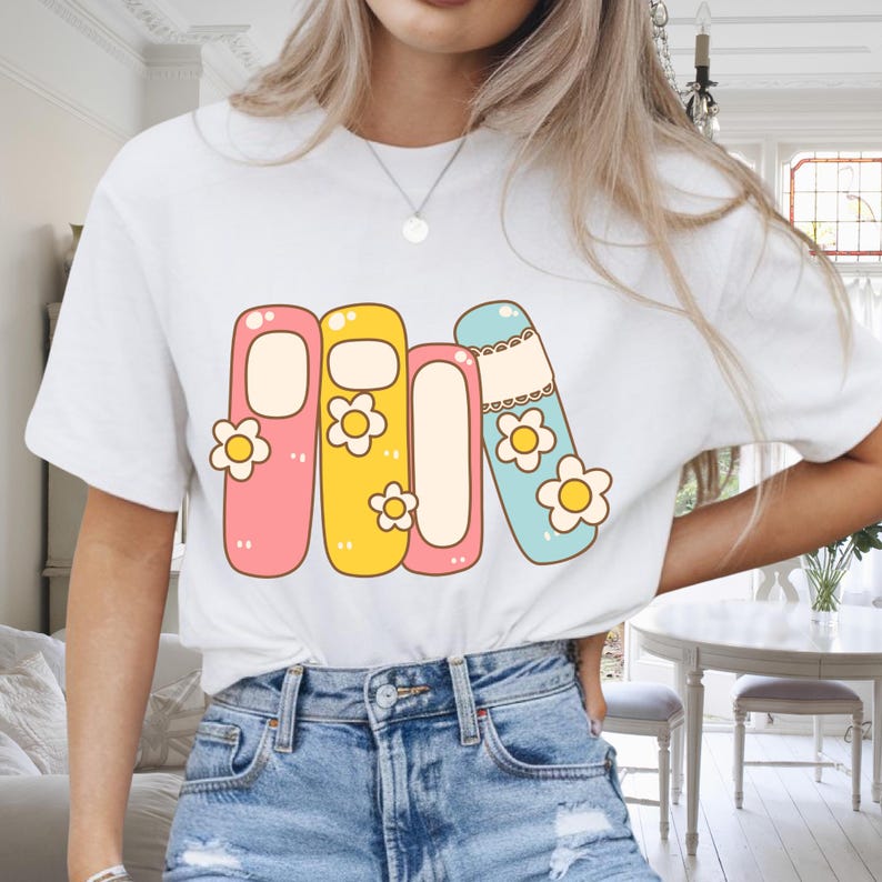 Może przedstawiać: Biały t-shirt z kolorową grafiką przedstawiającą cztery stylizowane książki w kolorze r&oacute;żowym, ż&oacute;łtym i niebieskim, każda ozdobiona stokrotką. Projekt nadrukowany na klasycznym t-shircie z okrągłym dekoltem.