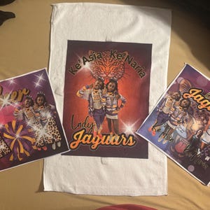 May include: Three custom printed items featuring cheerleading graphics. A white towel with a central image of two cheerleaders and the text "Lady Jaguars". Two smaller prints with cheerleaders, the word "Cheer", and the text "Ke'Asia Ke'Naria".
