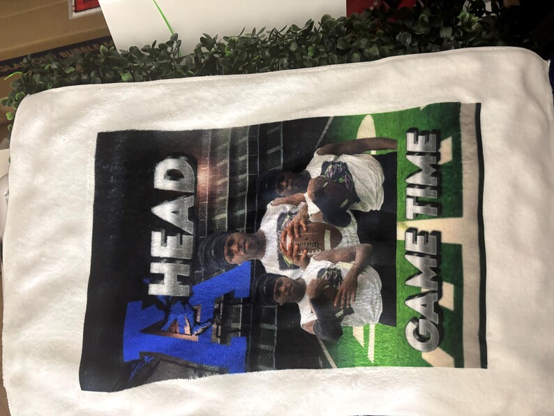 May include: White rectangular towel with a printed image of a football team. The image features players in white shirts and black caps, holding a football. The words "HEAD" and "GAME TIME" are printed on the towel.