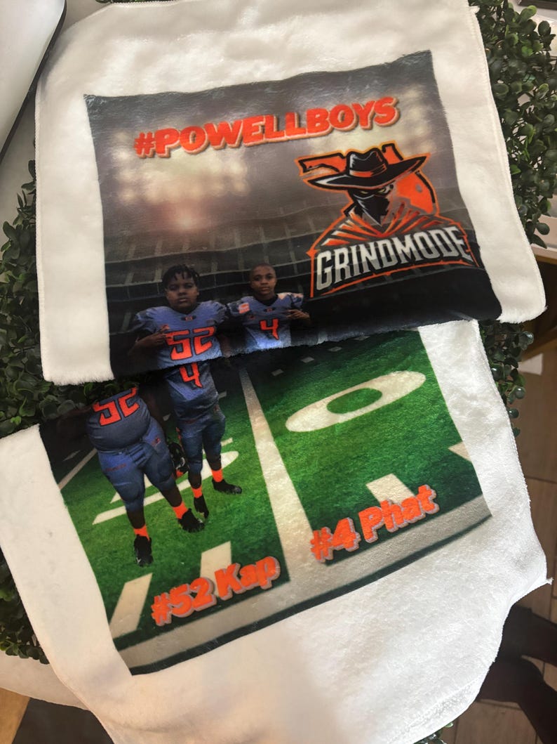 May include: White plush towels with a football field design. One towel features the text "#POWELLBOYS" and a graphic of a masked cowboy. The other towel shows two football players on a green field with the text "#52 Kap" and "#4 Phat".