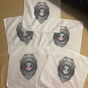 May include: Five white square cloths with a printed security badge design. The badge is silver with the words "COLLINS SECURITY" and a central emblem featuring a building and the words "LIBERTY & JUSTICE FOR ALL".