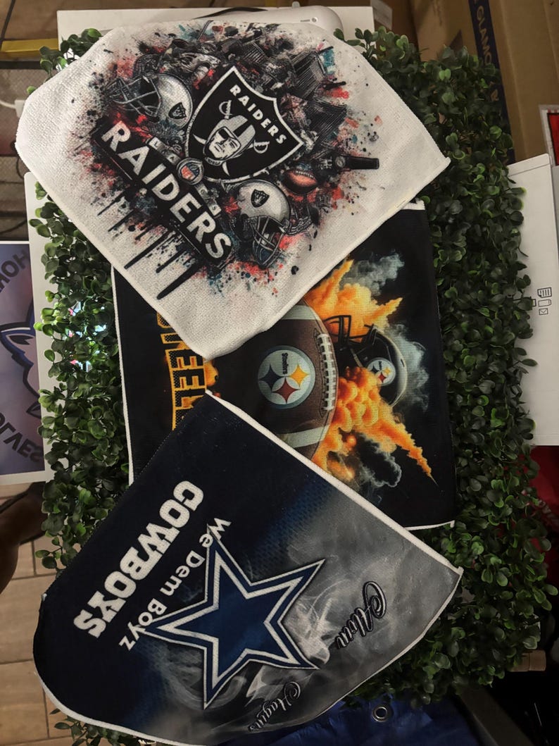 May include: Three sports-themed items: a white Raiders towel with the team logo and helmets, a black Steelers towel with a football and flames, and a navy Cowboys towel with a star and text.