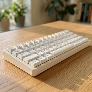 Peut inclure: Un clavier mécanique blanc au format compact, doté de touches affichant à la fois des caractères latins et des hiragana japonais imprimés en noir. Le clavier présente un cadre rectangulaire épuré et une disposition standard de type QWERTY.