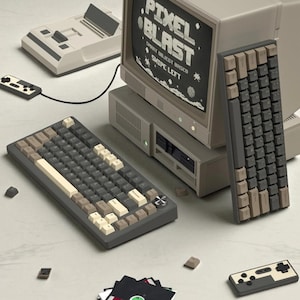 May include: A retro computer setup featuring a monitor displaying "Pixel Blast" text, two keyboards with gray, beige, and white keys, a game console, a controller, and floppy disks. The color scheme is primarily gray and beige.