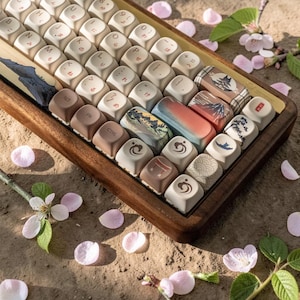 May include: A custom mechanical keyboard with Japanese-themed keycaps. The keycaps feature various designs, including landscapes, birds, and Japanese characters. The keyboard is housed in a wooden frame, and the scene is decorated with pink flower petals.
