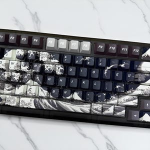 May include: A black mechanical keyboard with custom keycaps featuring a wave design in shades of white, gray, and black. The keyboard has function keys and a number pad. The keycaps have a glossy finish.