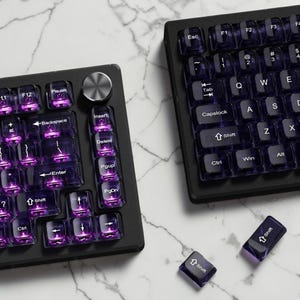 May include: Two black mechanical keyboards with translucent purple keycaps and white lettering are shown on a marble surface. The keyboards have function keys, including Esc, Ctrl, Shift, and Enter. Two loose Shift keycaps are also visible.