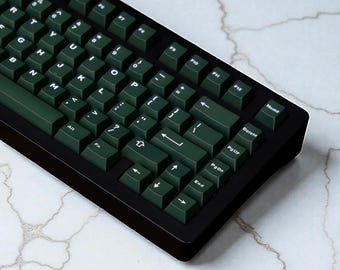 May include: A black mechanical keyboard with dark green keycaps. The keyboard has a standard layout with letters, numbers, and function keys. The keycaps are a solid, dark green colour with white lettering. The keyboard is angled slightly towards the user.