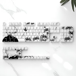 May include: White mechanical keyboard with black and white anime-style graphics. The keycaps feature a design of a person, flowers, and rain. A unique and artistic accessory for any computer setup.