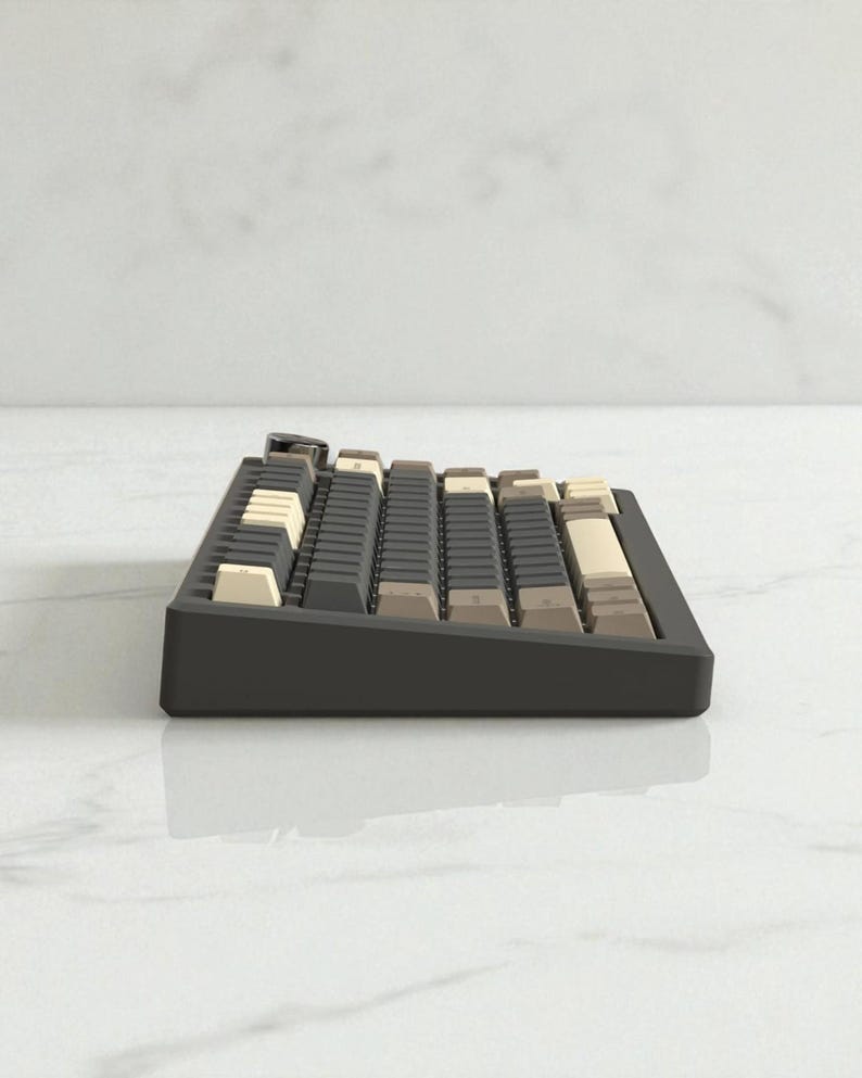 May include: A side view of a black mechanical keyboard with a variety of keycap colors, including beige, gray, and brown. The keyboard sits on a white surface, reflecting its form.
