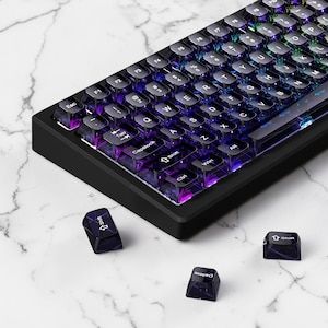 May include: Black mechanical keyboard with transparent keycaps. The keys are backlit with a rainbow of colours. Three detached keycaps are scattered nearby. The keyboard has a black frame and a compact design.